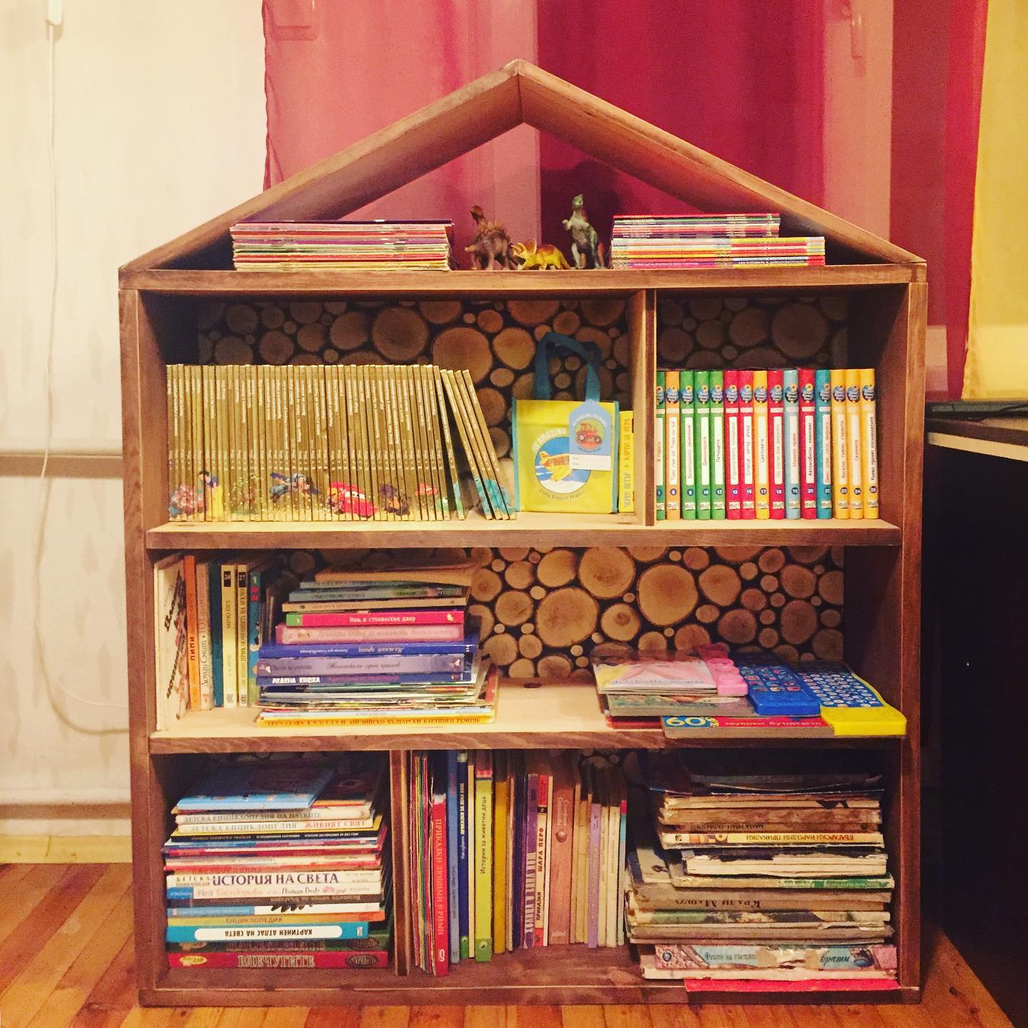 The finished wooden bookshelf filled with children's books, with toy dinosaurs arranged on the top.
